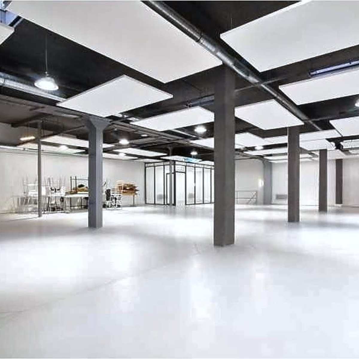 A spacious, empty room with white walls, a polished floor, and several hanging ceiling panels.