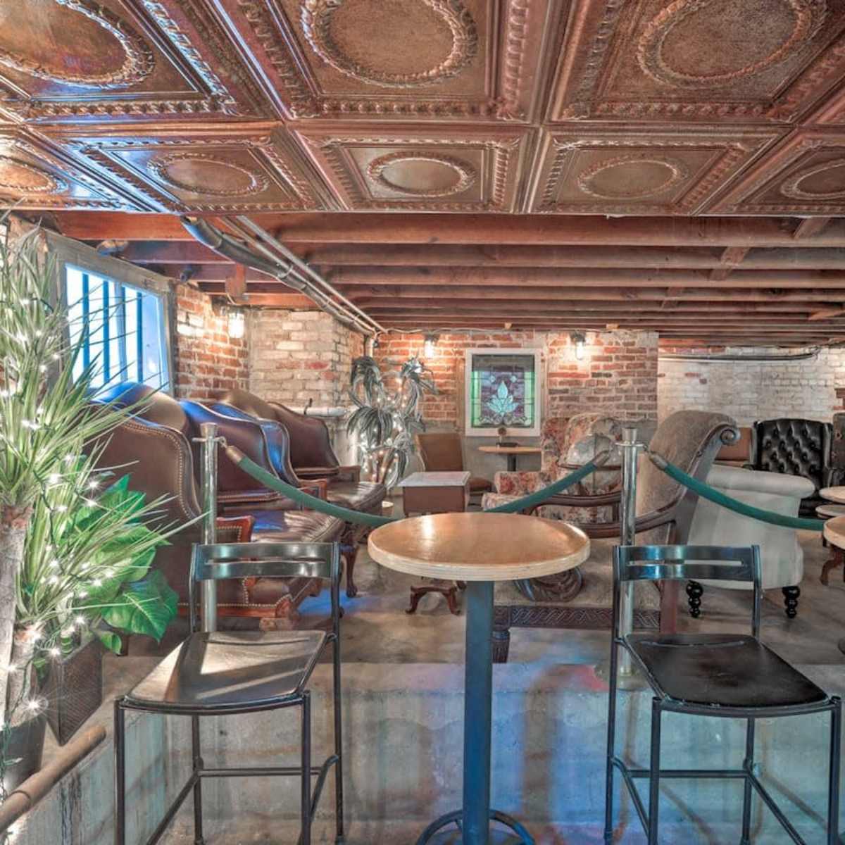 A rustic bar area with wooden stools, exposed brick walls, and a tin ceiling in a dimly lit space.