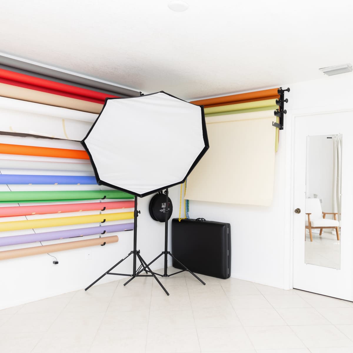 A photography studio with a wall of colorful backdrop rolls, a large lighting umbrella, and storage space containing white materials.
