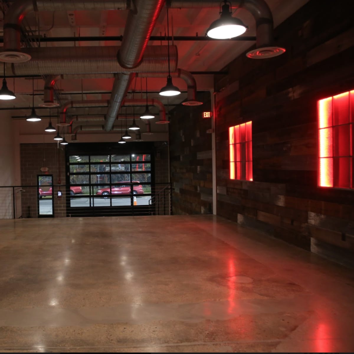 An empty, industrial-style interior space with exposed ductwork, pendant lights, and wooden wall accents.