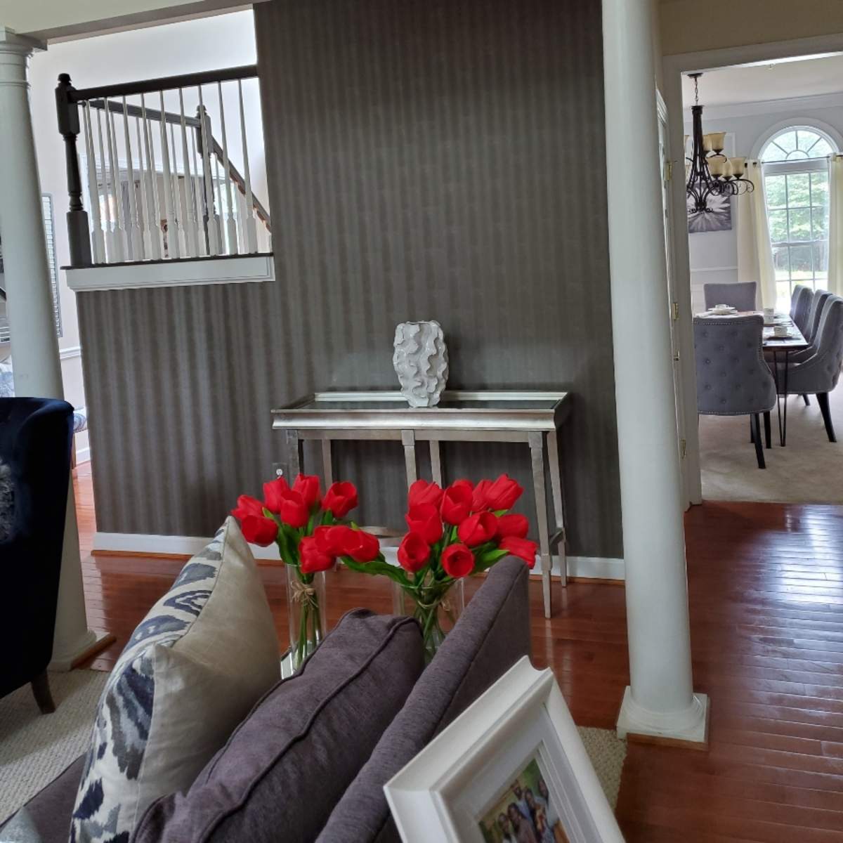 A living room with a console table and a vase of red tulips against a striped wallpaper backdrop, framed by two white columns.