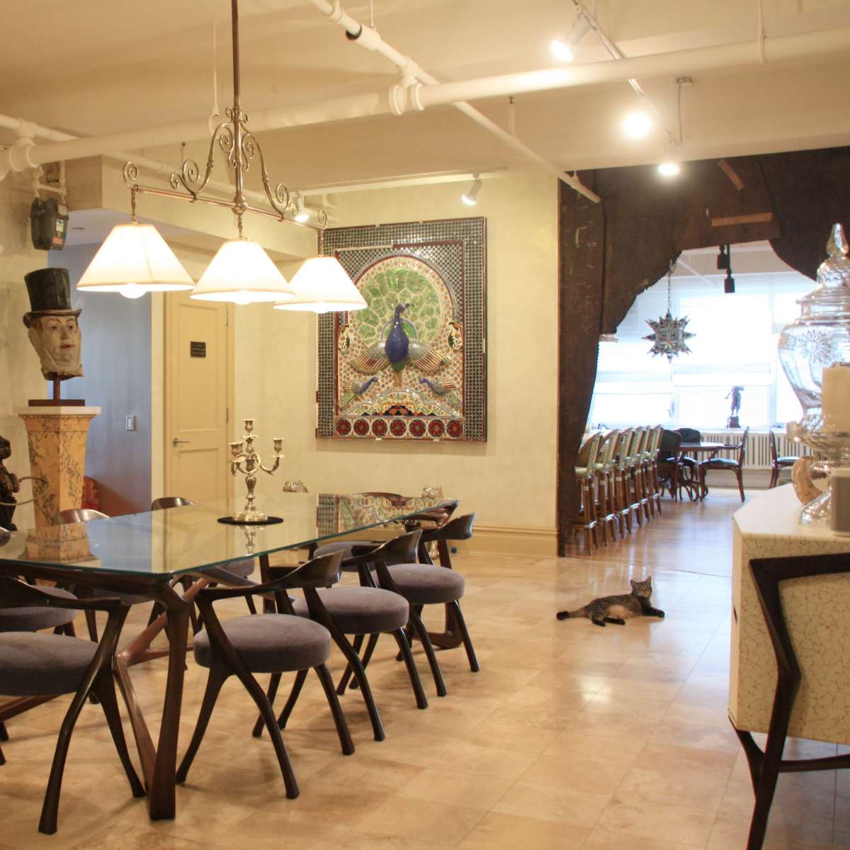 A spacious dining area with a glass-top table surrounded by upholstered chairs, ornate artwork on the walls, and various decorative items throughout the room.