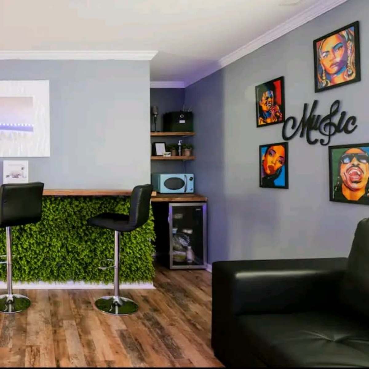 A modern interior with a bar area featuring four black stools, a wall covered in greenery, and framed portraits of musicians.