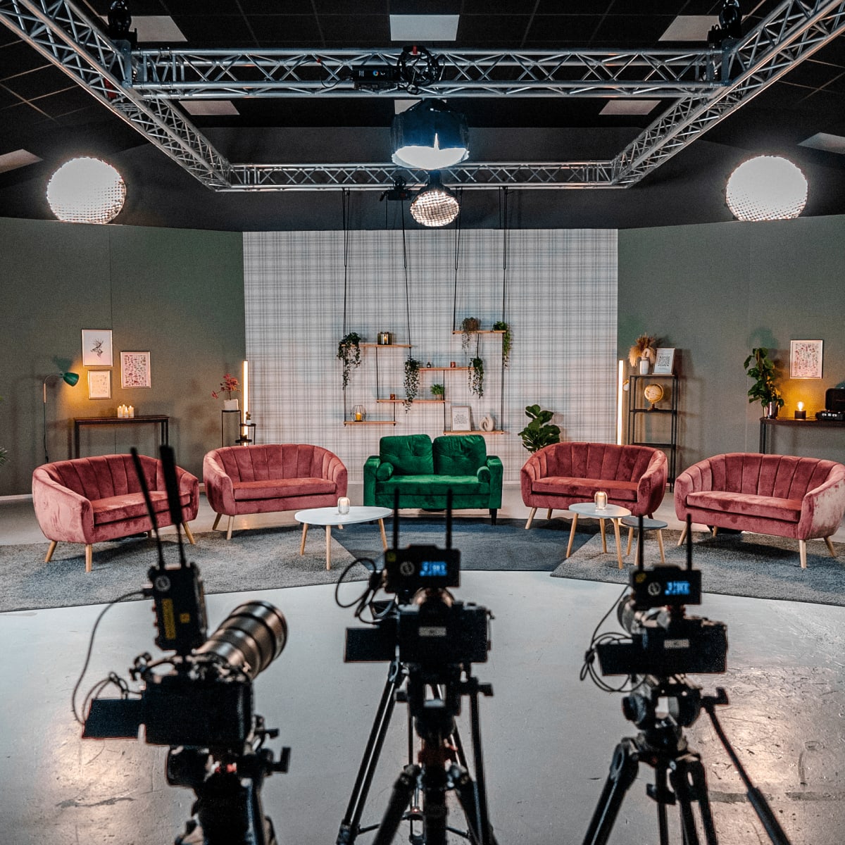 A television studio set features multiple sofas arranged in a semi-circle with cameras positioned in front.