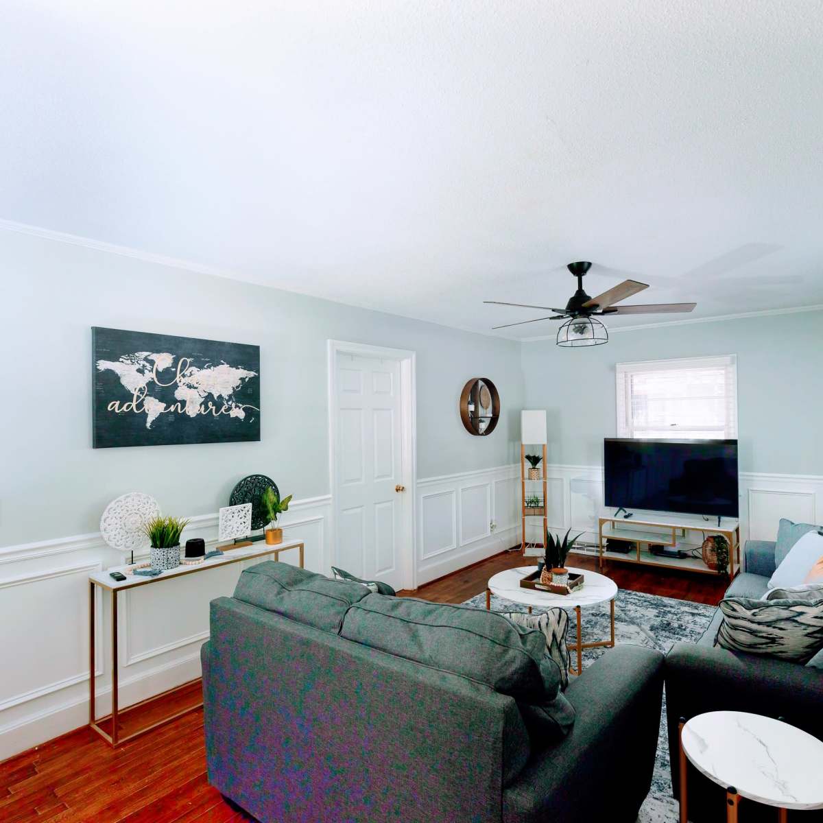 A living room with a gray sofa, a small round table, a TV on a stand, and a map artwork on the wall.