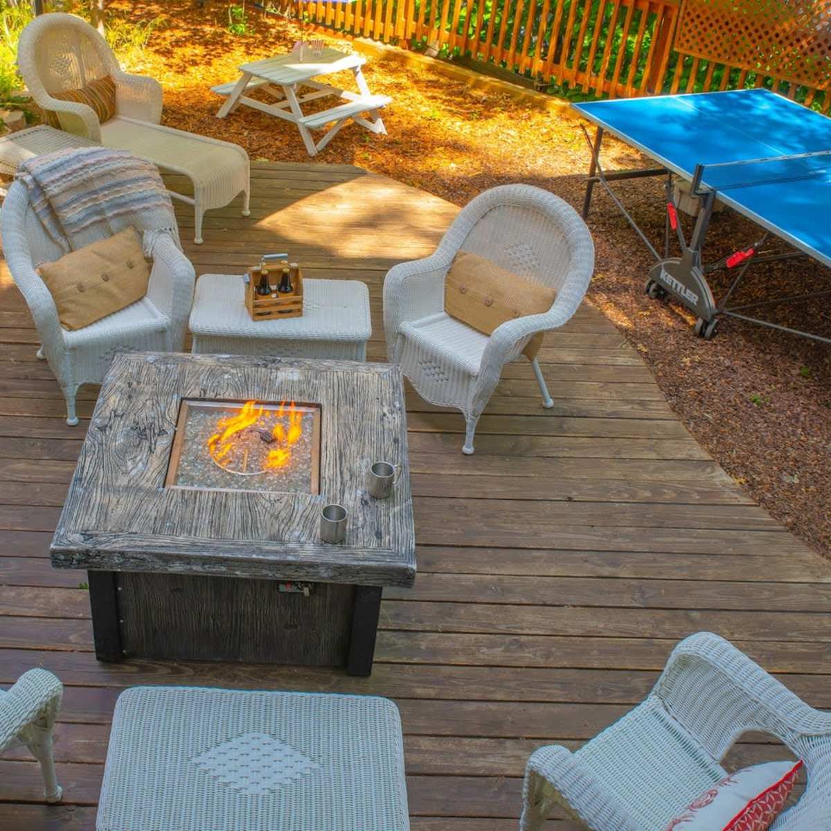 A patio area with a fire pit surrounded by white wicker chairs and a table tennis setup in the background.