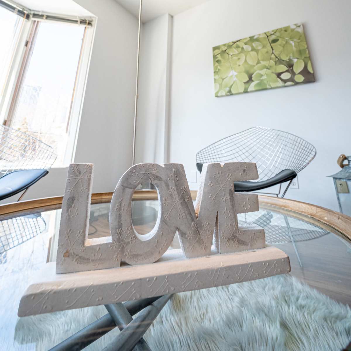 A decorative statue spelling "LOVE" sits on a glass table under a pendant light in a bright, modern room.