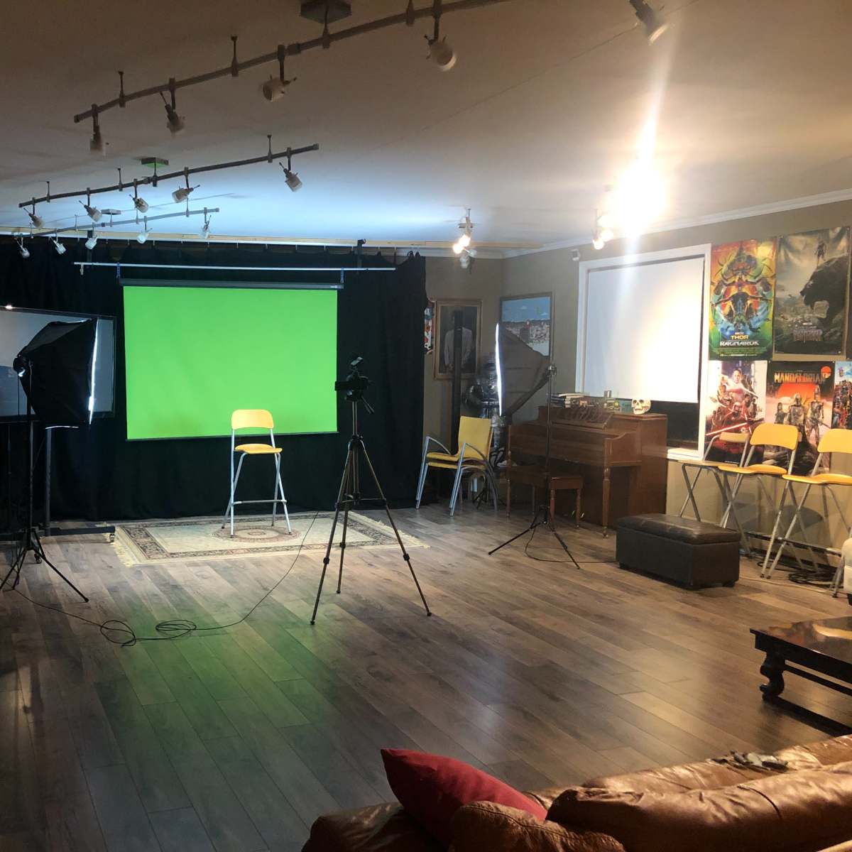 A spacious studio setup with a green screen at the center, flanked by cameras and lighting equipment, along with rows of chairs arranged for an audience.