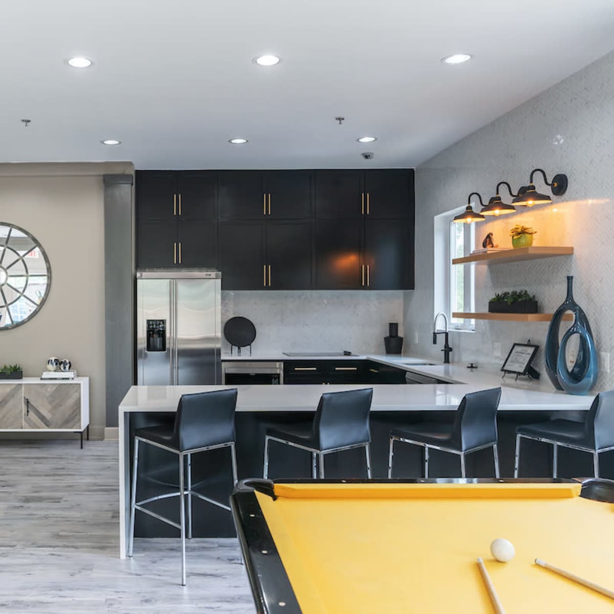 A modern kitchen and lounge area with black cabinetry, a large mirror, and a pool table visible in the foreground.