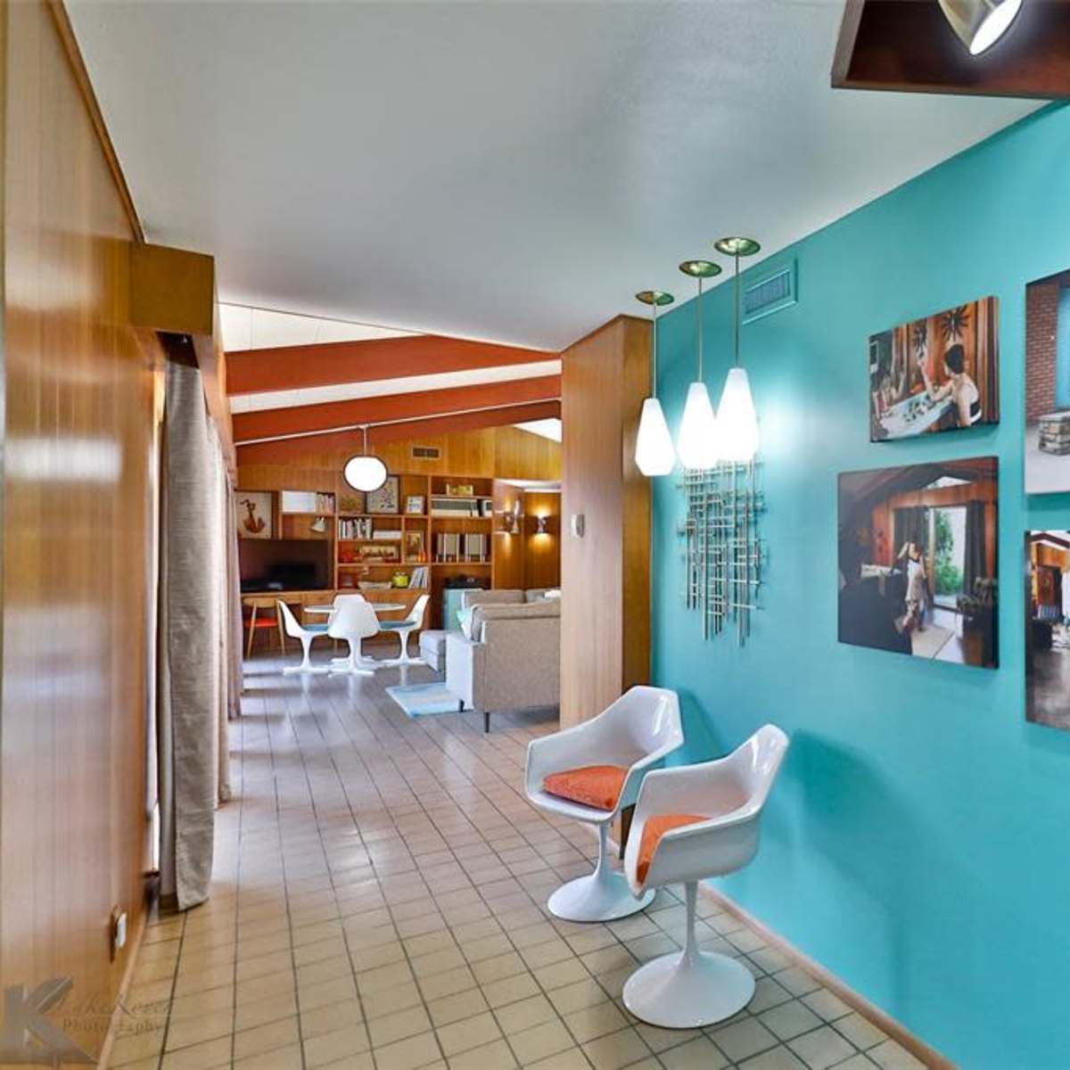 A brightly colored hallway with a blue wall featuring framed photographs, leading towards a living area with light-colored furniture.