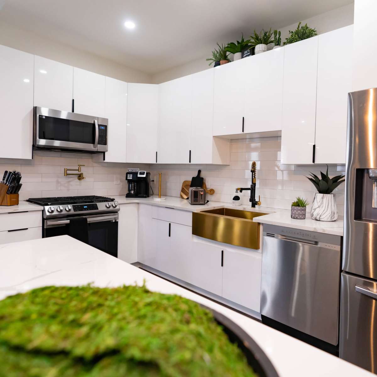 A modern kitchen features stainless steel appliances, white cabinetry, and a gold sink.