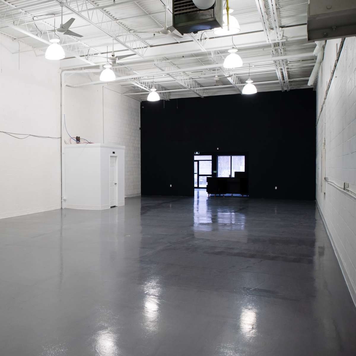 An empty, spacious room with a polished gray floor, white walls, and a contrasting black wall at one end.