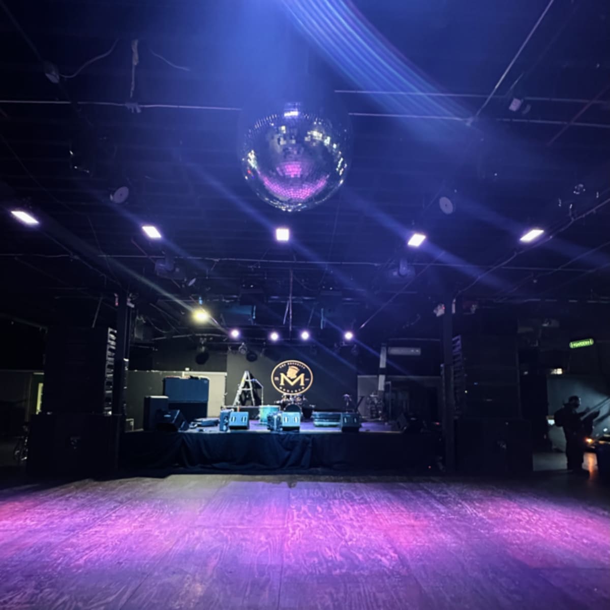 An empty music venue featuring a stage with a disco ball and lights, set against a dark floor.