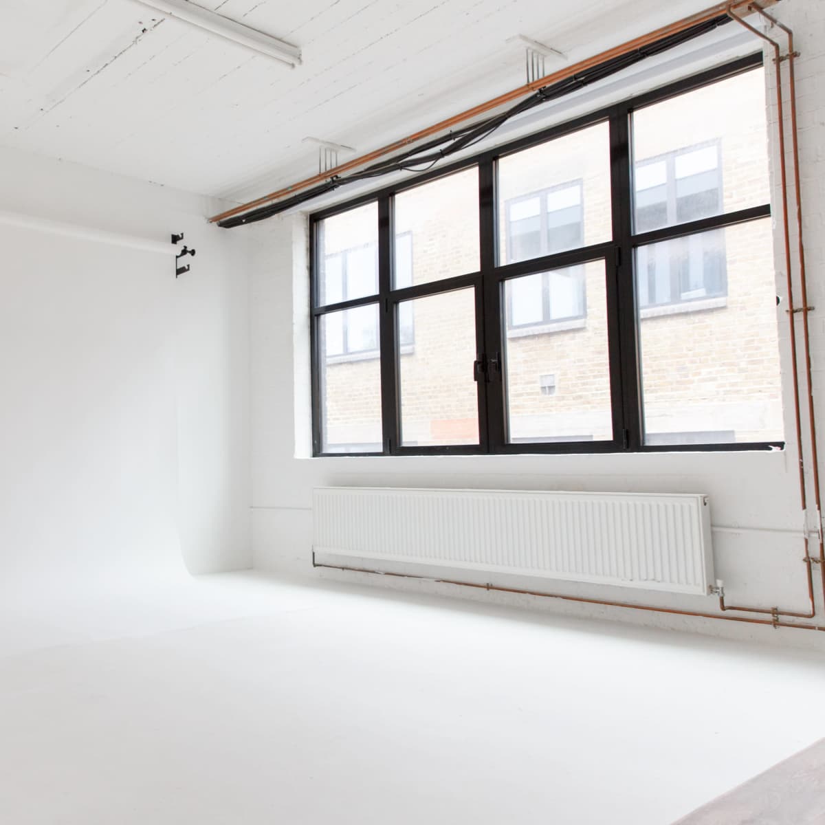 A bright, empty photography studio with a white backdrop and large windows letting in natural light.