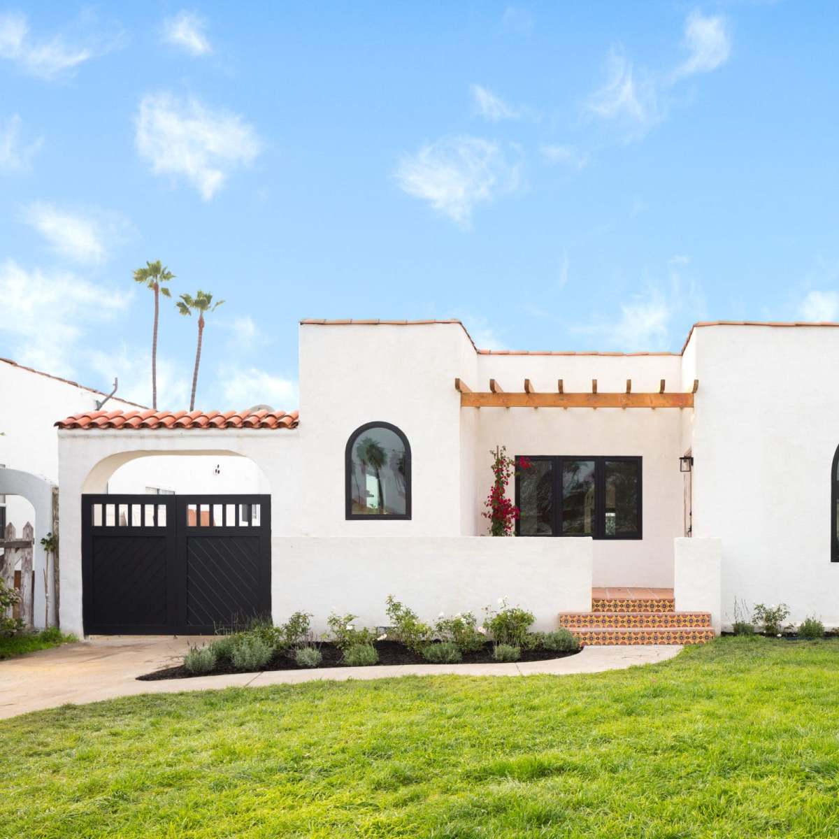 A white stucco house with arched windows, a tiled roof, and a landscaped front yard.