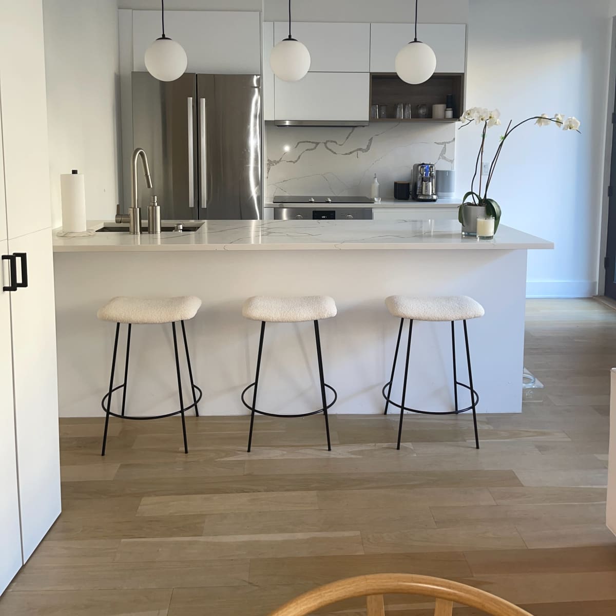 A modern kitchen features a central island with three bar stools, pendant lights above, and stainless steel appliances.