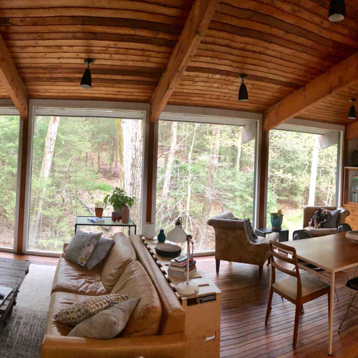 A spacious living area with wooden beams and large windows overlooking a wooded landscape.