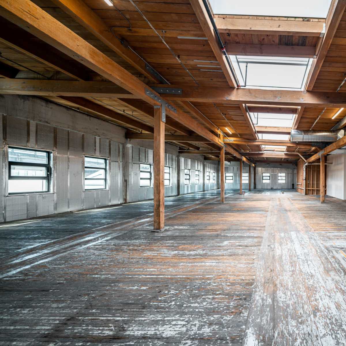 A spacious interior of a renovated industrial building with wooden beams and large windows.