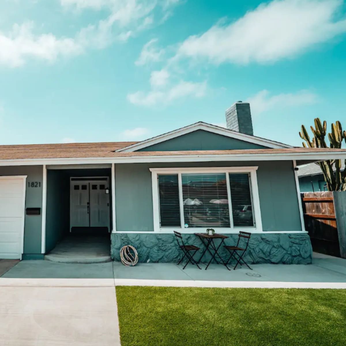 A single-story gray house with a two-car garage, a small front lawn, and outdoor seating on the porch.