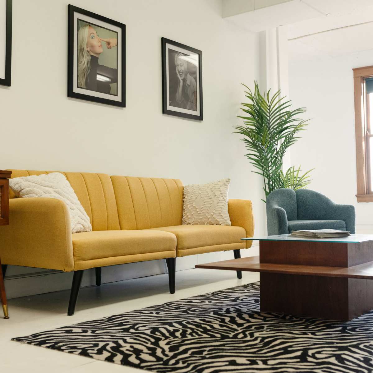 A modern living room with a yellow sofa, a green armchair, and a low wooden coffee table on a zebra-striped rug, surrounded by framed artwork on the walls.