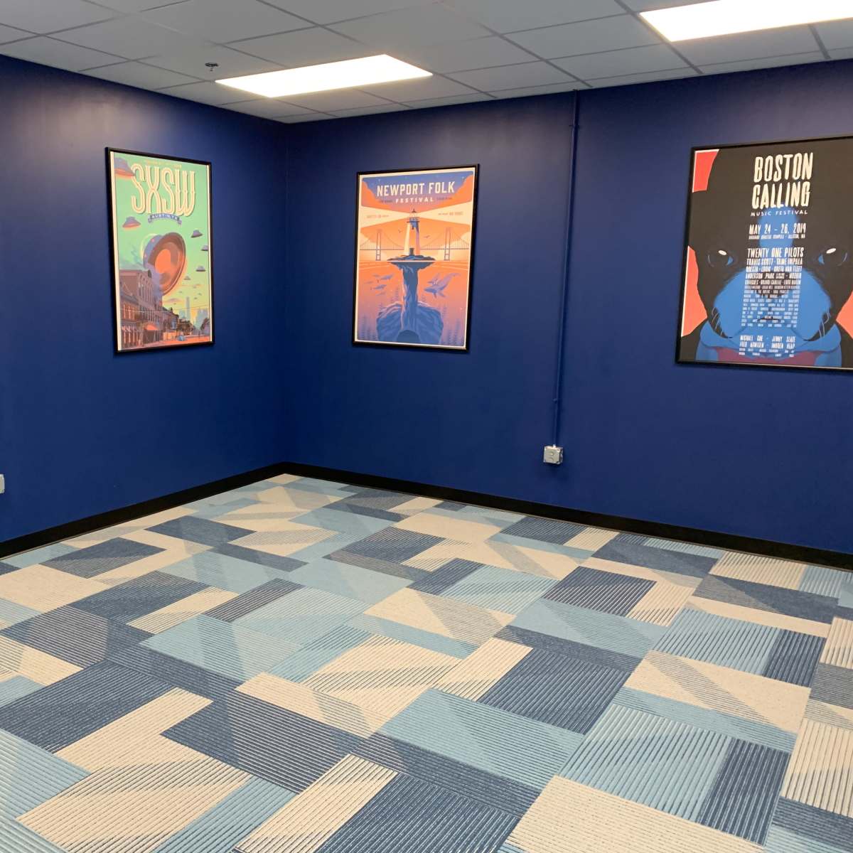 A room with blue walls, a patterned carpet in shades of blue, and framed posters on the walls.