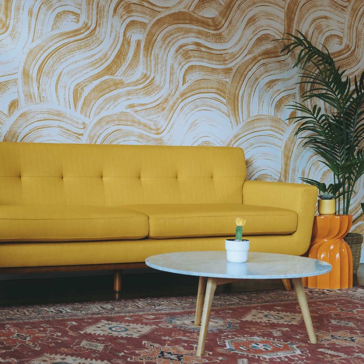 A yellow sofa is positioned in front of a textured, wavy golden wall, accompanied by a round coffee table and potted plants.