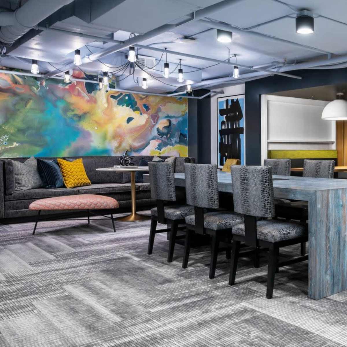 A modern coworking space featuring a long table with black chairs, colorful wall art, and private booth seating areas.