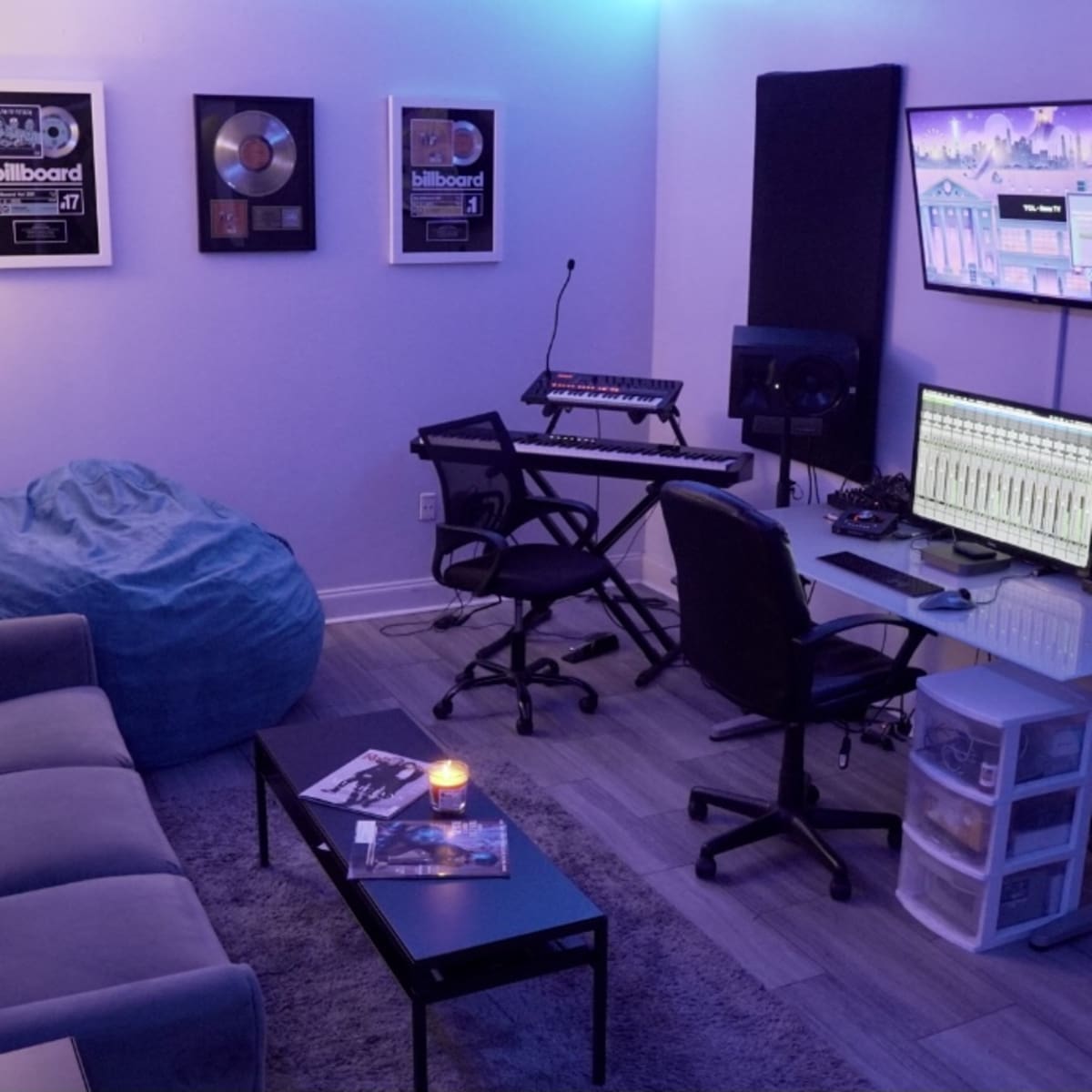 A music production studio with a sofa, a table with equipment, a computer setup, and ambient lighting.
