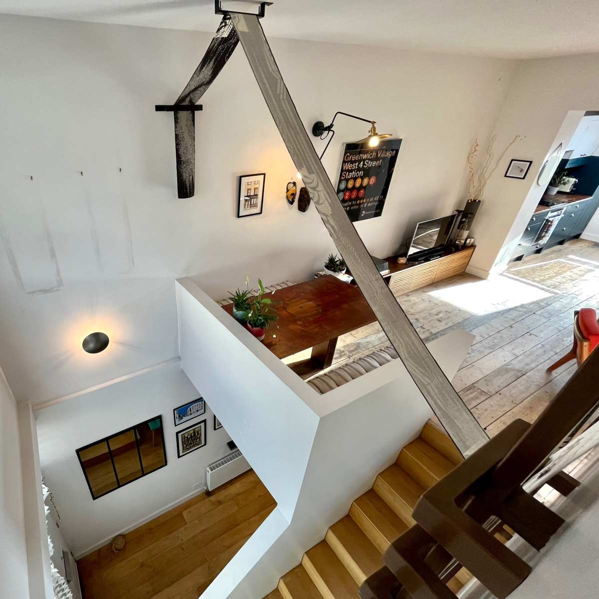 An interior space with a staircase leading down to a dining area, featuring a wooden table and wall-mounted decor.