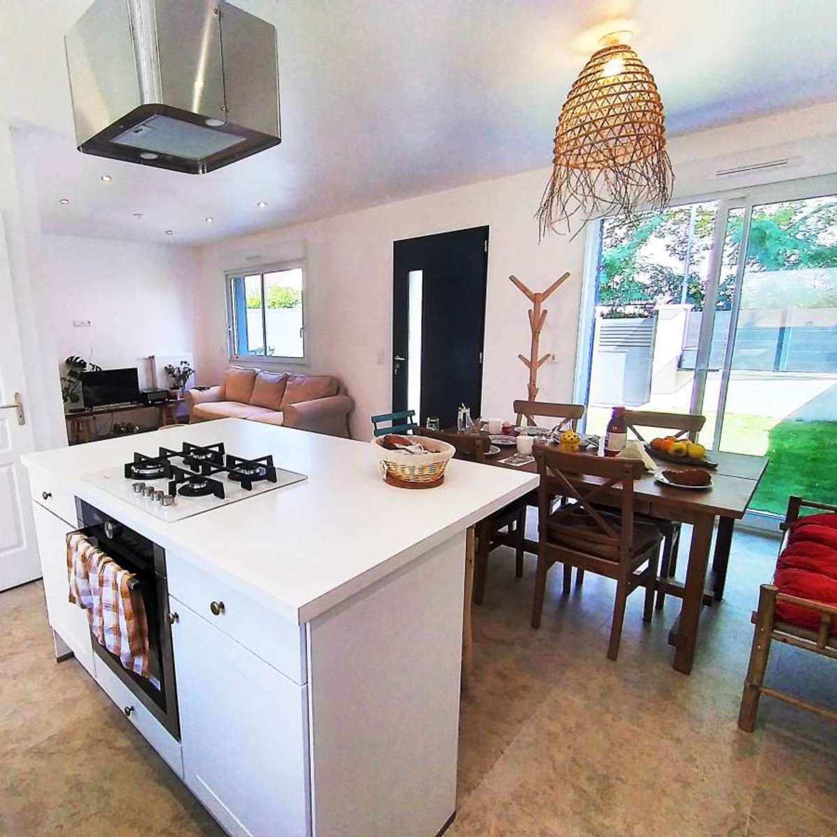 A modern kitchen with an island, gas stove, dining area, and large windows that open to a backyard.