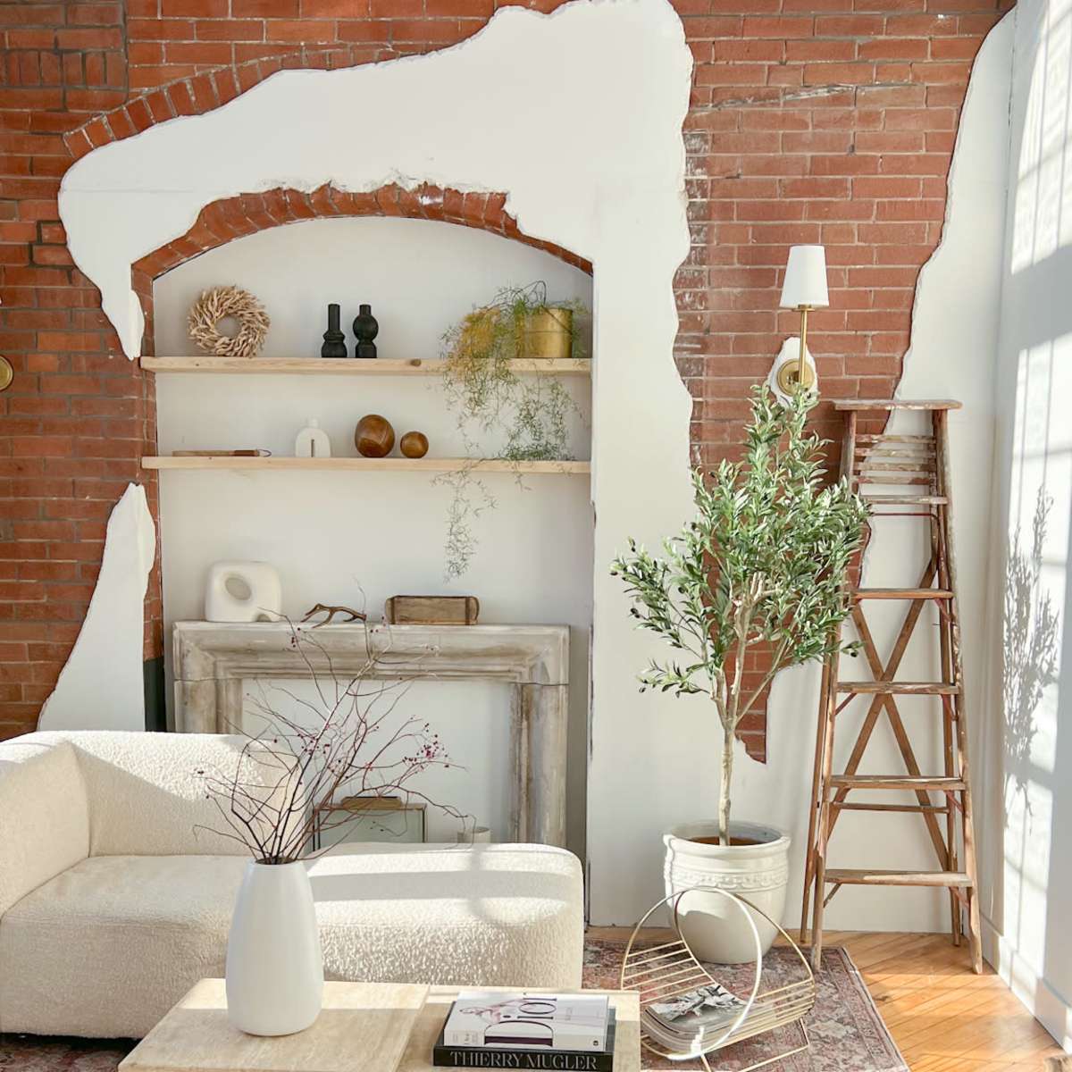 A well-lit living room with a white couch, wooden coffee table, and a brick wall featuring a partially removed section, showcasing a shelf with decorative items.