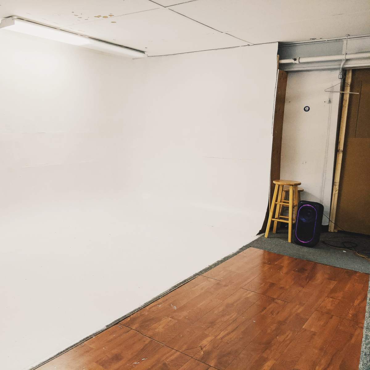 An empty room with a white backdrop, a wooden stool, and a purple speaker in the corner.