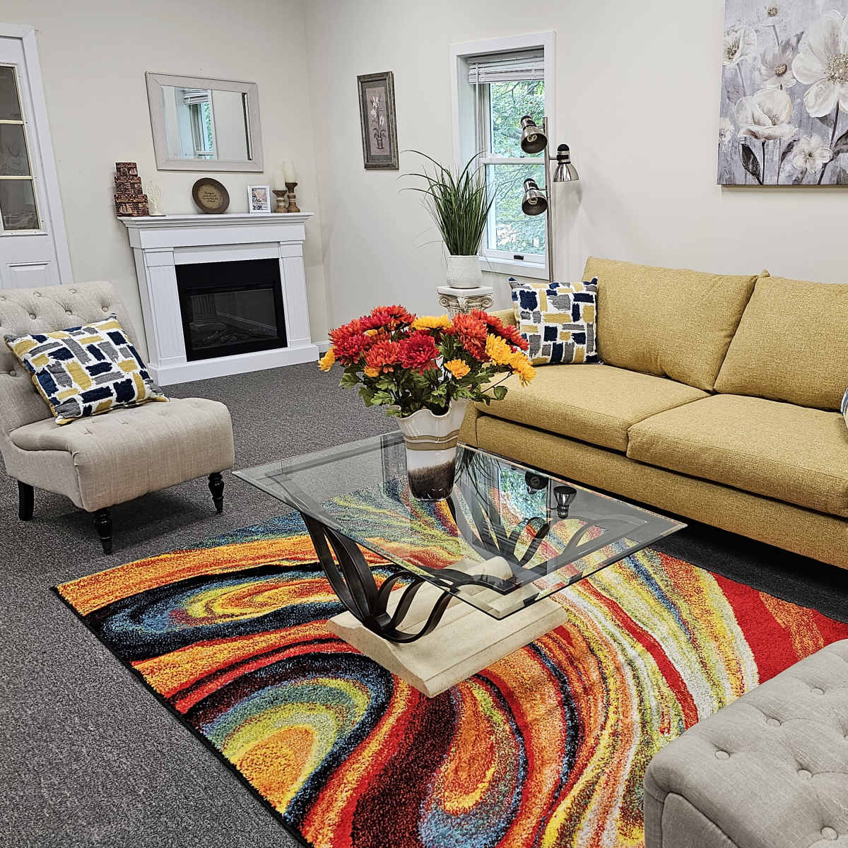 A cozy living room with a yellow sofa, two accent chairs, a glass coffee table, and a colorful swirling rug.