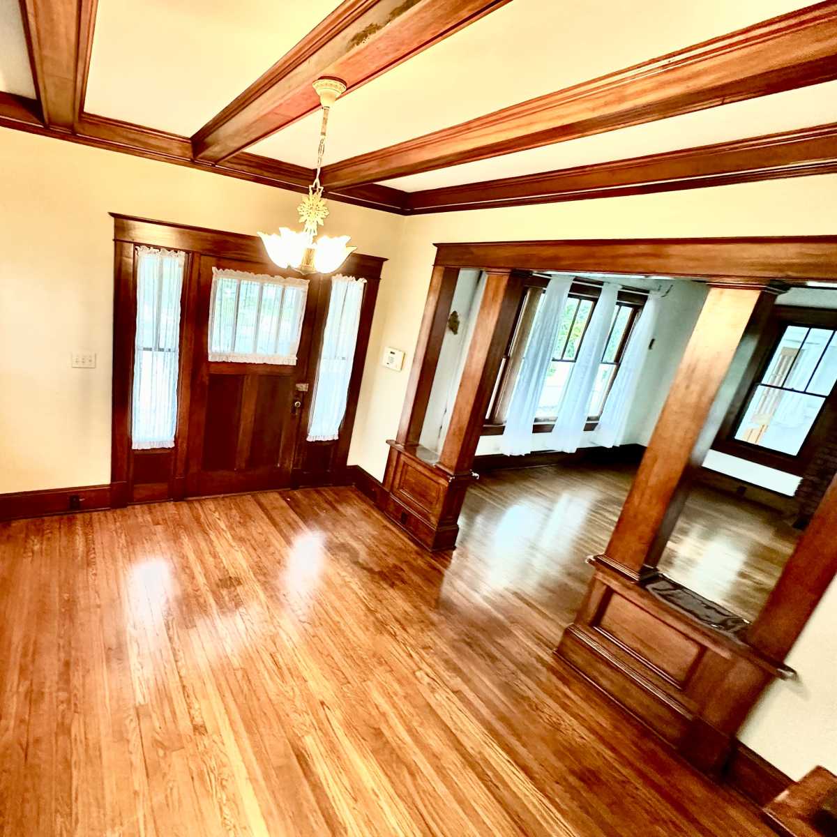A room with wooden beams on the ceiling, hardwood floors, and several windows with shutters.