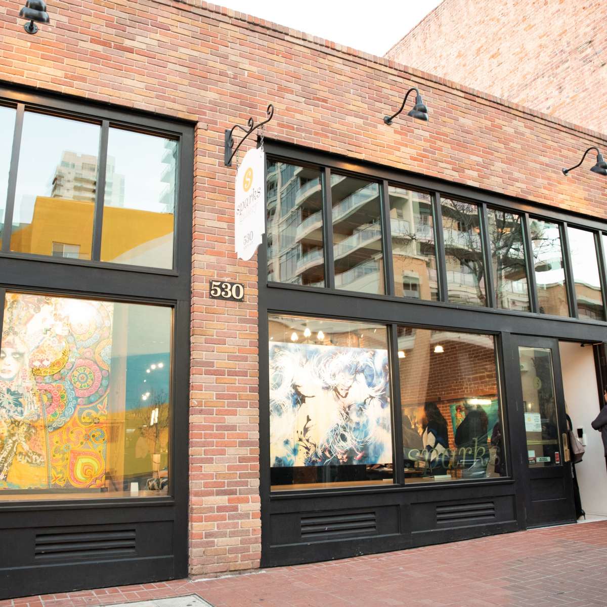 A brick building with large windows displaying colorful artwork, and a person entering through the door.