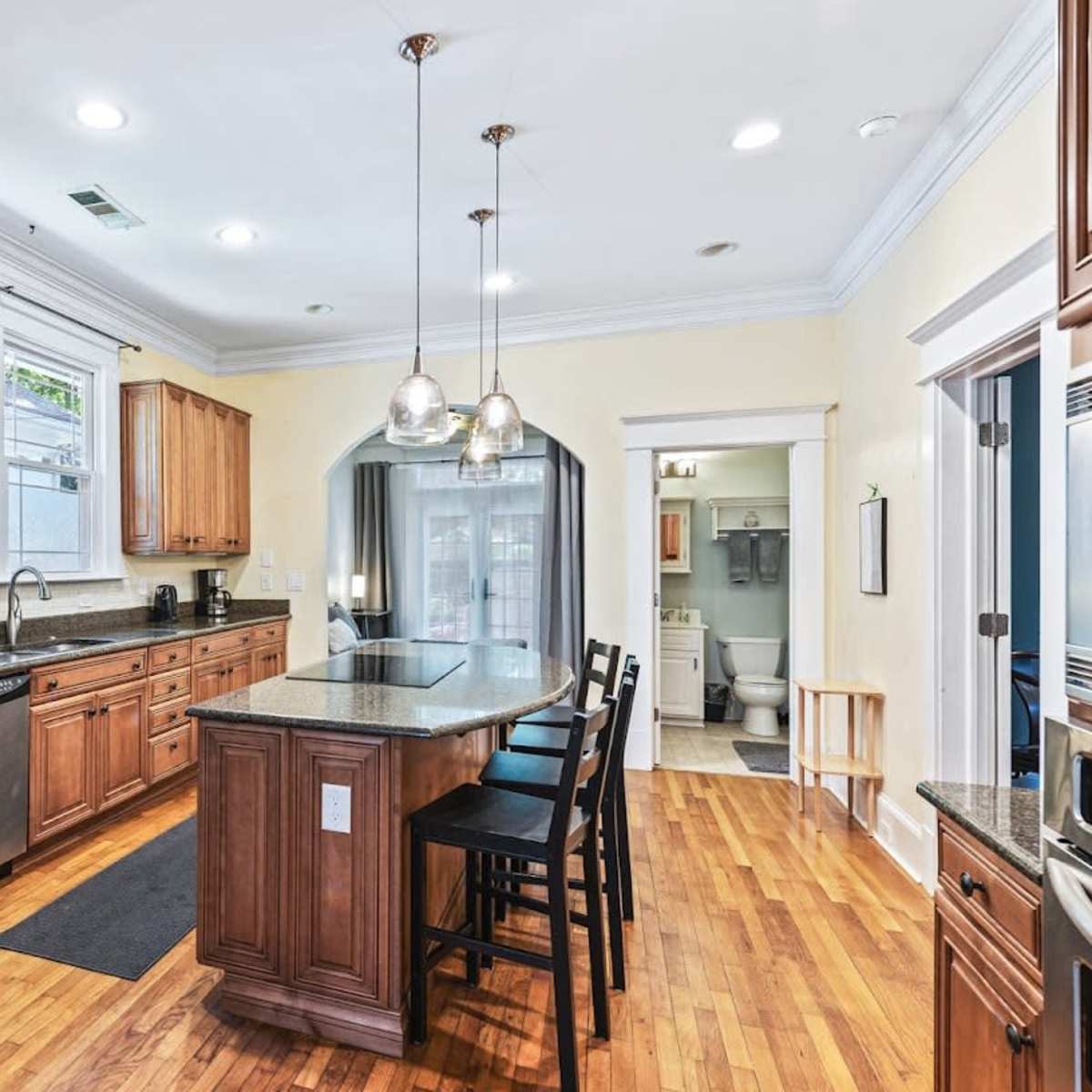 A modern kitchen features wooden cabinets, stainless steel appliances, a large island with seating, and a doorway leading to a bathroom.