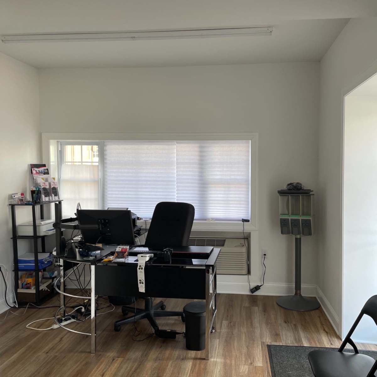 A minimalistic office space featuring a black desk with a computer, a chair, and a bookshelf, along with a small waiting area with two chairs.