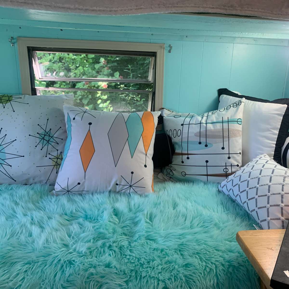 A cozy sleeping area features a collection of colorful pillows and a fluffy blue blanket beneath a window.