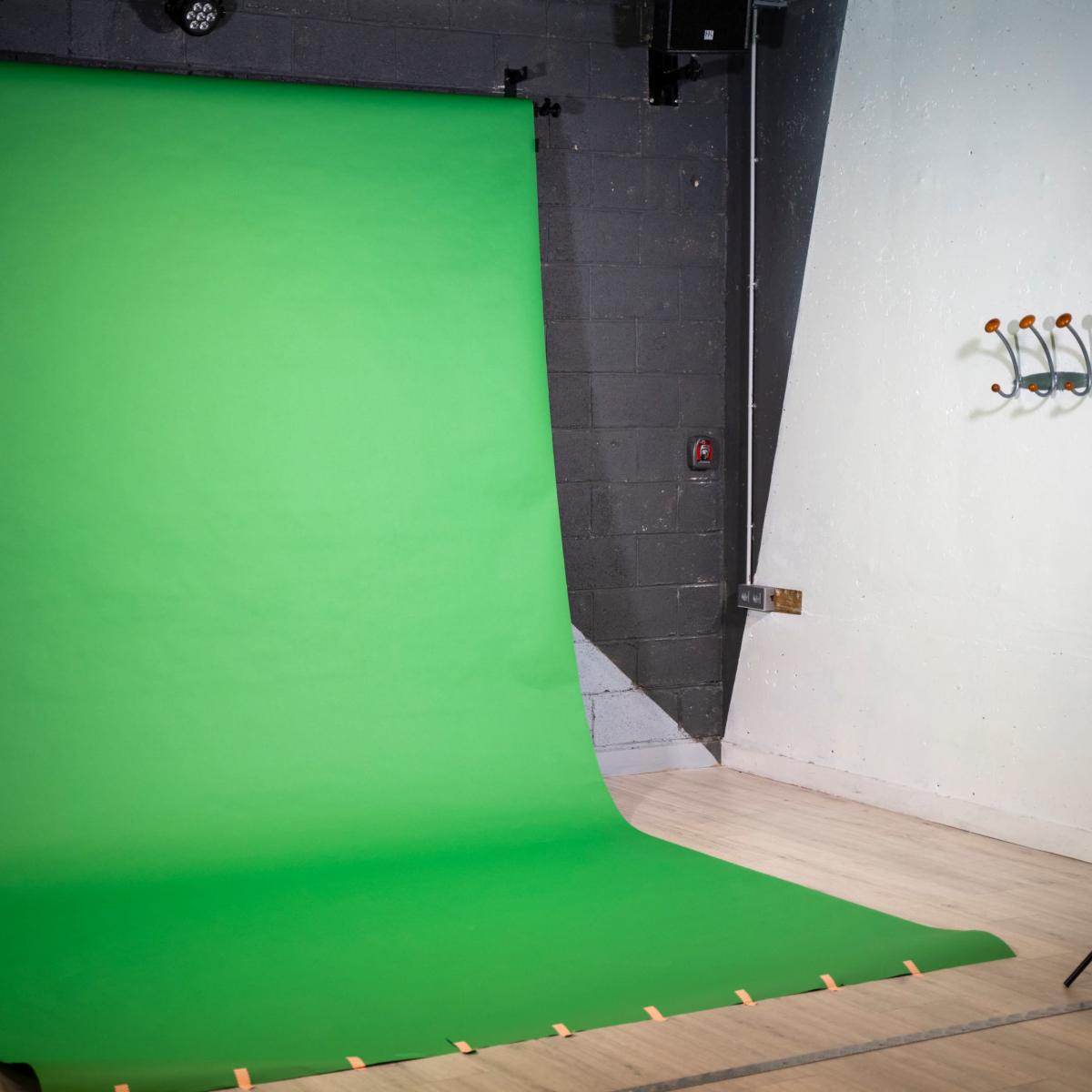 A studio setup featuring a large green backdrop, two lights on stands, and a wall with hooks.