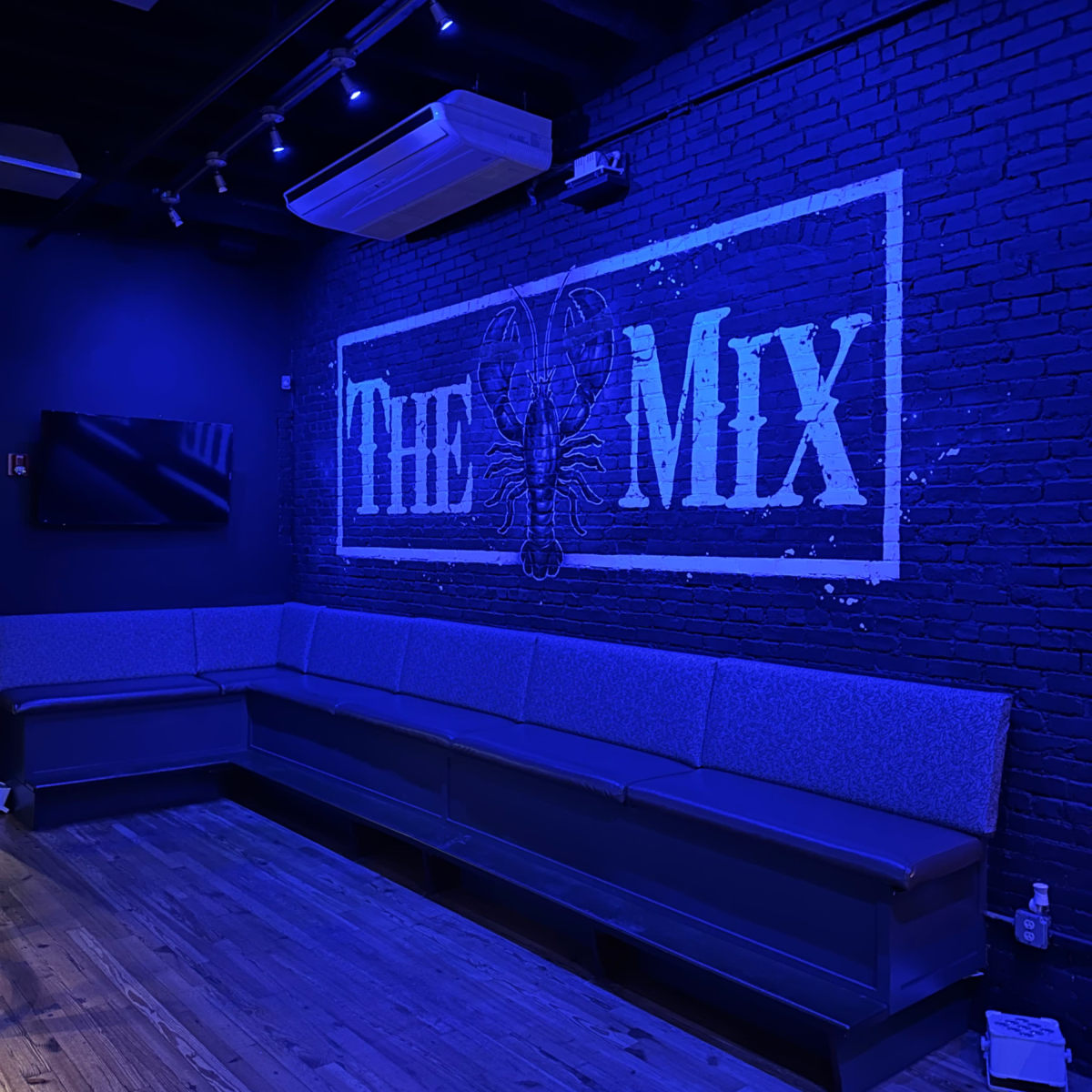 A dimly lit lounge area with a large blue mural reading "THE MIX" on a black brick wall and a long gray couch along the side.