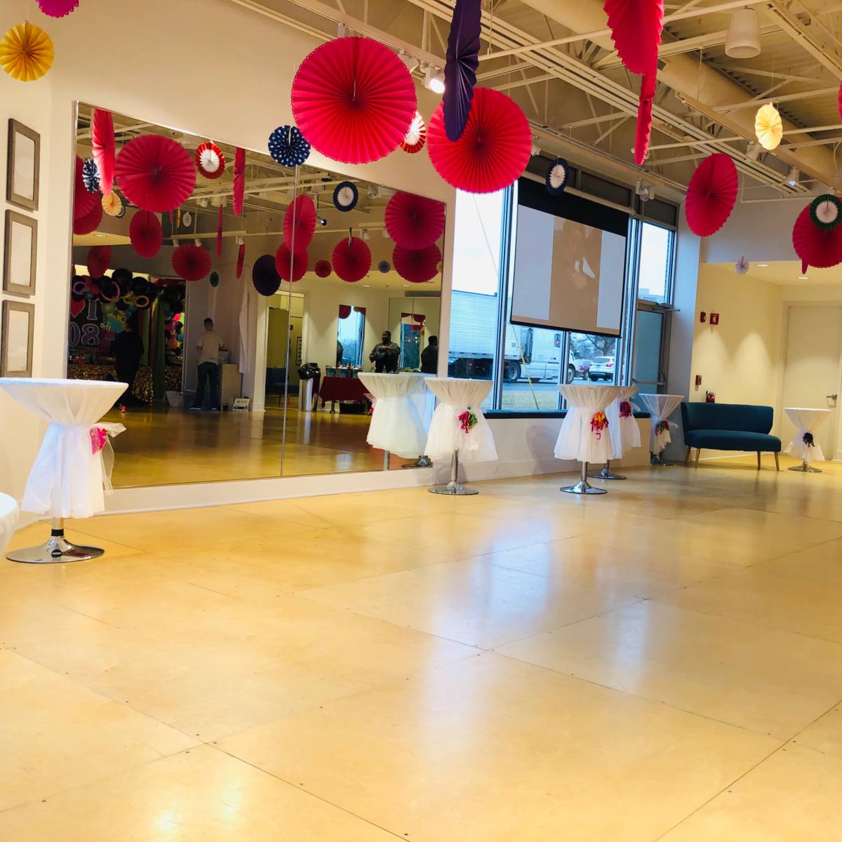 A spacious event room with decorated walls, colorful paper decorations hanging from the ceiling, and several tables set up with white tablecloths.