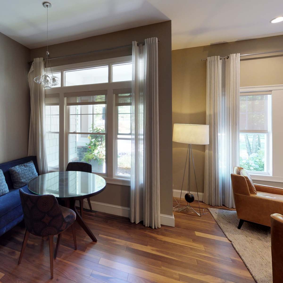 A small sitting area featuring a blue couch, a round glass table, and two wooden chairs with a window providing natural light.