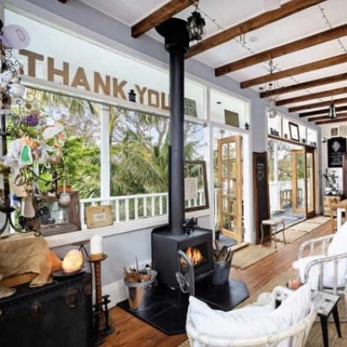 A spacious living area with wooden beams, a black stove, and a dining table surrounded by various decorative items and plants.