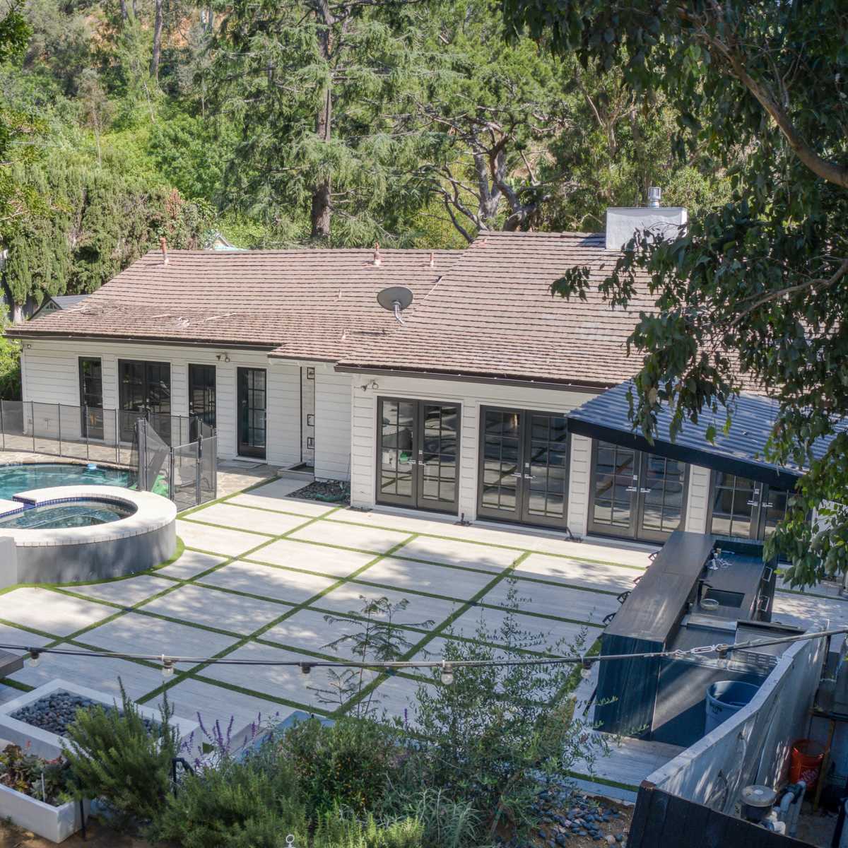 A modern single-story house with a landscaped backyard featuring a spa, seating area, and pathway surrounded by greenery.