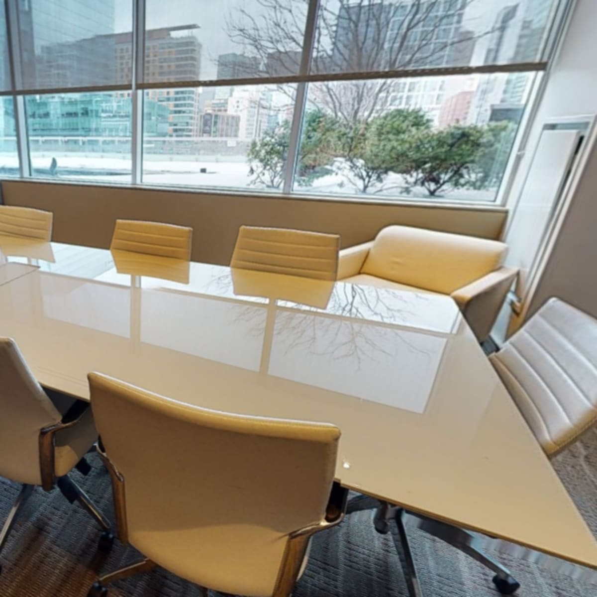 A modern conference room with a long white table and eight chairs, overlooking a cityscape through large windows.