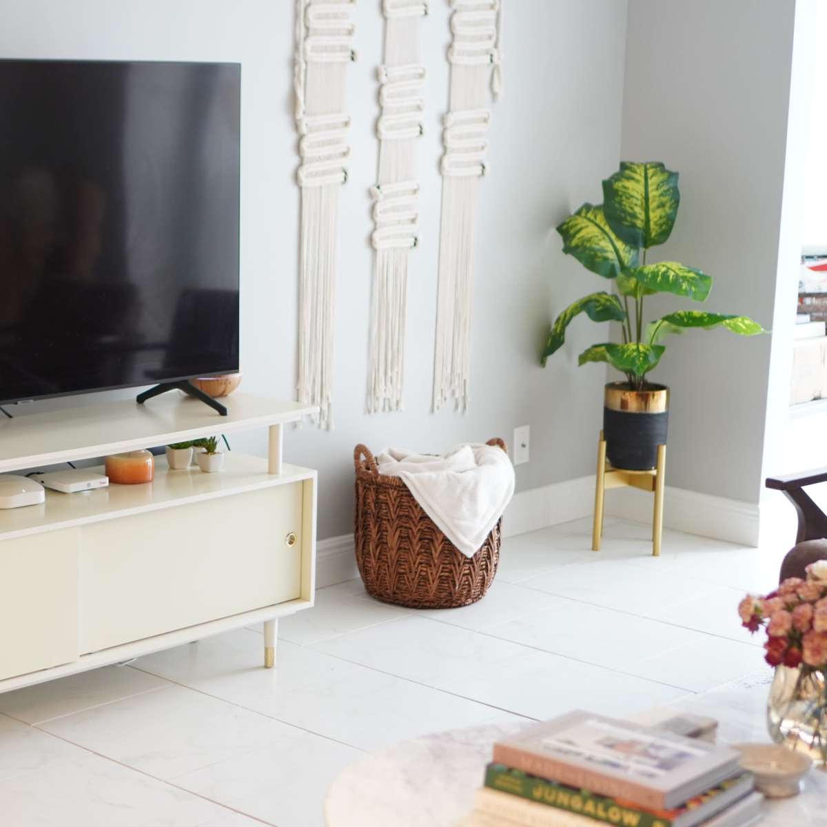The scene features a modern living room with a large flat-screen TV mounted above a light-colored entertainment unit, accompanied by a decorative basket and a potted plant.
