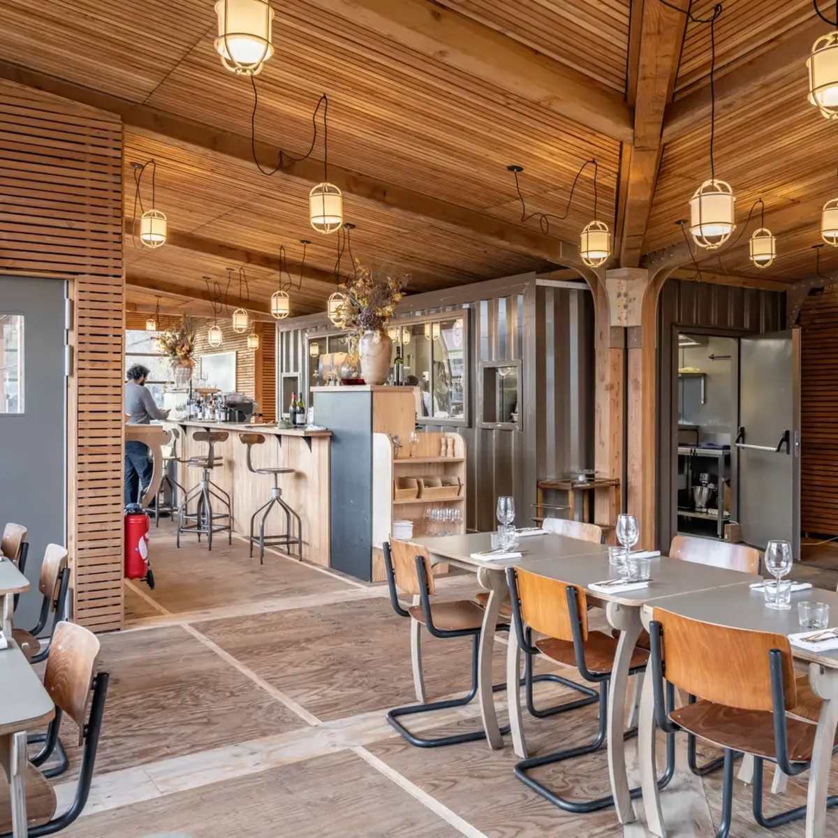 The interior of a restaurant featuring wooden beams, pendant lighting, and tables set for dining.