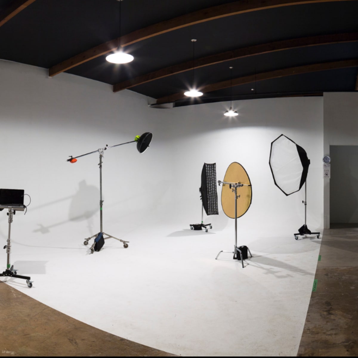 A photography studio with a seamless white backdrop, several lighting equipment setups, and a small bar table in the corner.