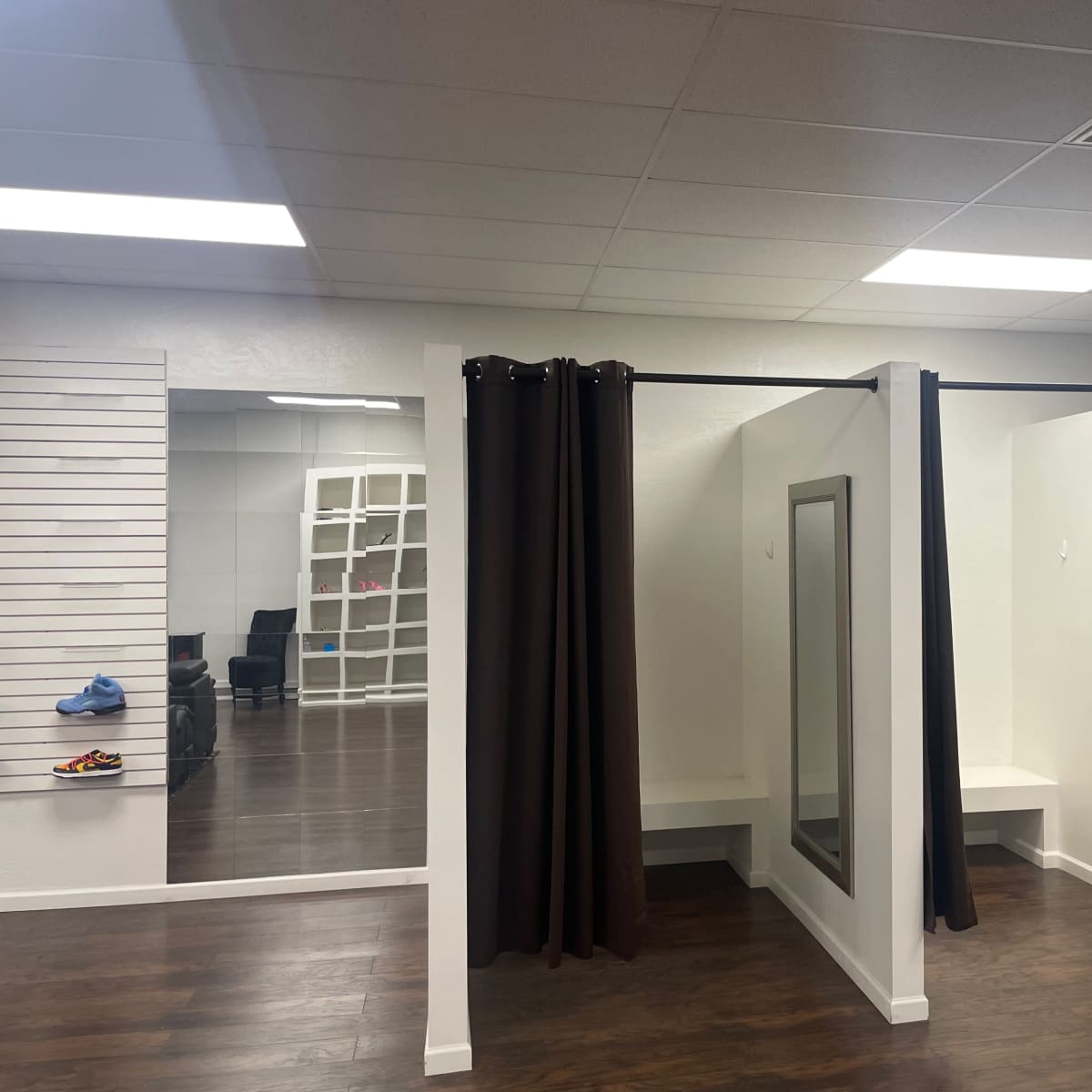 A sparse fitting room area with three enclosed changing stalls, a full-length mirror, and a neatly organized display area.