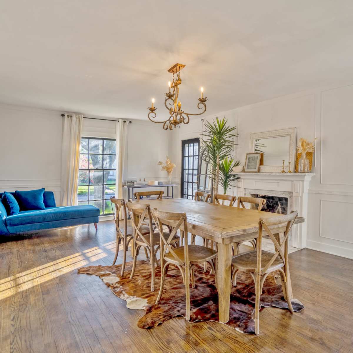 A dining area features a wooden table surrounded by chairs, a blue couch in the corner, and a chandelier hanging from the ceiling.